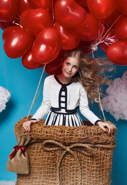 Kleines süßes Mädchen, das auf roten Herzballons zum Valentinstag fliegt — Stockfoto