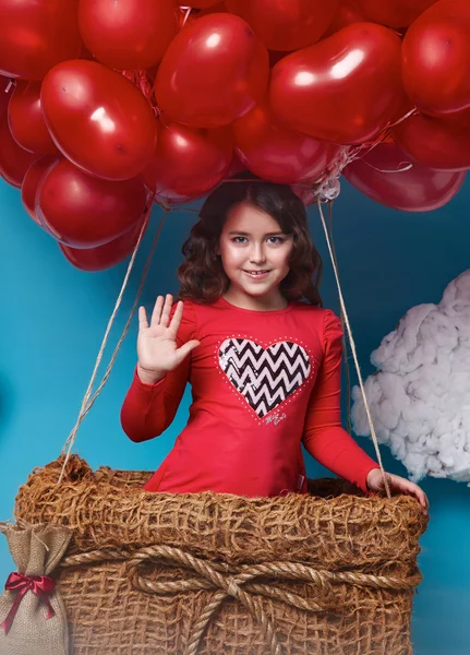 Pequena menina bonito voando em balões de coração vermelho dia dos namorados — Fotografia de Stock