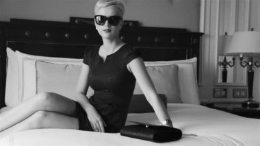 Lüks otel yatak odasında sıska kısa elbise takı güneş gözlüğü giyen güzel seksi sarışın iş kadını içki şarap toplantı dan önce dinlenmek moda trendi kırmızı ruj yastık çarşafları makyaj yapmak