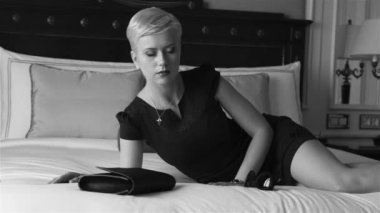 Lüks otel yatak odasında sıska kısa elbise takı güneş gözlüğü giyen güzel seksi sarışın iş kadını içki şarap toplantı dan önce dinlenmek moda trendi kırmızı ruj yastık çarşafları makyaj yapmak
