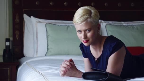 Krásná sexy blonďatá žena v hubených krátkých šatech šperky v luxusním hotelovém pokoji Odpočívej odpočinek módní trend před schůzkou nápoj víno vytvořit červený polštářek rtěnky — Stock video