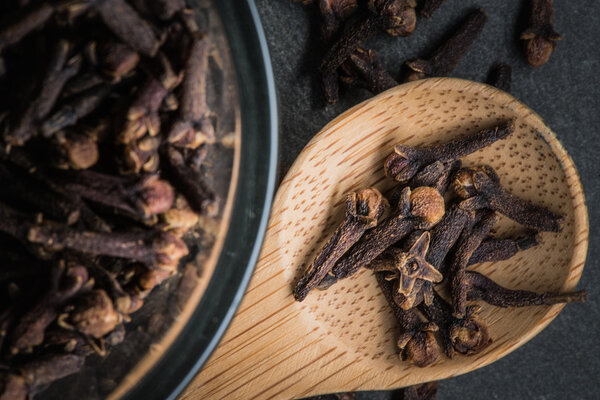 Wooden Spoon of Cloves sitting next to Glass Bowl of Cloves