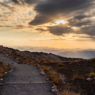 Washington Dağları üzerindeki bulutların arasında parlayan güneş, geniş toprak patikalar oluşturur.