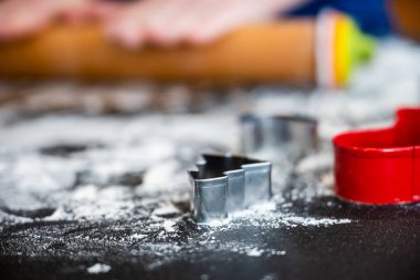 Minik Noel Kurabiyesi kesicileri, un kaplı yüzeyde arkalarında merdaneyle otururlar.