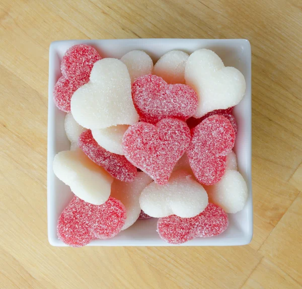 Corazones de goma roja y blanca en un tazón blanco en un bloque de carnicero — Foto de Stock