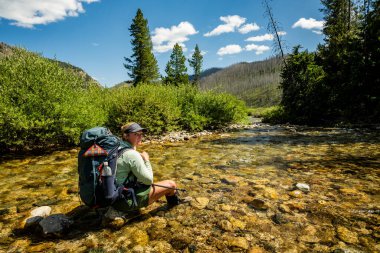 Sırt çantası Grand Teton Ulusal Parkı 'nda derede otururken geriye bakıyor