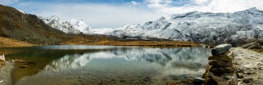Büyük Cairn Stellisee 'nin yanında duruyor ve Matterhorn' u çevreleyen dağlarda taze kar manzarası var.