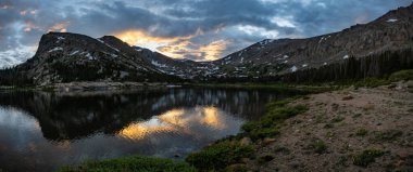 Akşam güneşi Rocky Dağı Ulusal Parkı 'ndaki Çim Gölü üzerindeki bulutları aydınlatıyor