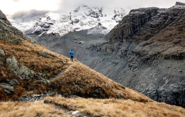 Adam sonbaharda İsviçre Alplerinde bir buzul vadisine bakıyor.