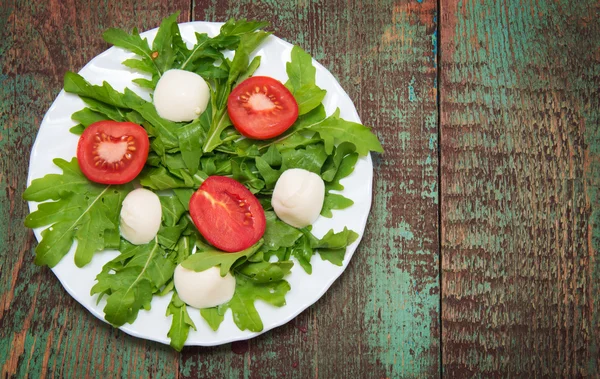 Groene salade gemaakt van arugula, tomaten, kaas mozzarella ballen en sesam op bord — Stockfoto