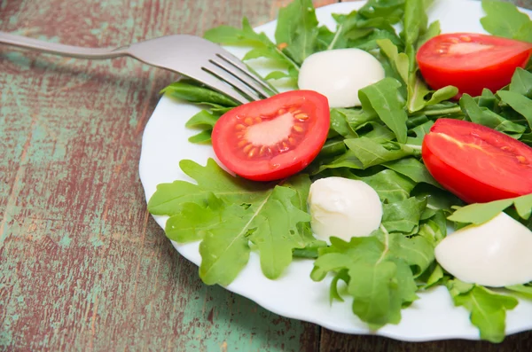 Groene salade gemaakt van arugula, tomaten, kaas mozzarella ballen en sesam op bord — Stockfoto