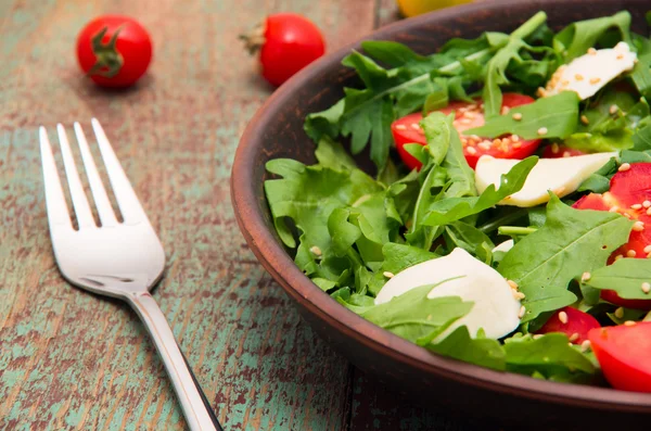 Green salad made with arugula, tomatoes, cheese mozzarella balls and sesame on plate — Stock Photo, Image