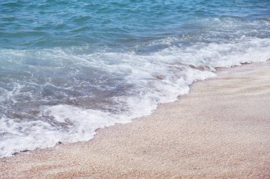 Kumlu sahilde yumuşak bir mavi deniz dalgası.