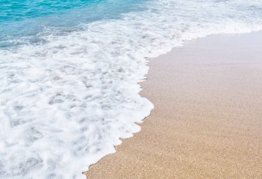 Kumlu sahilde yumuşak bir mavi deniz dalgası.