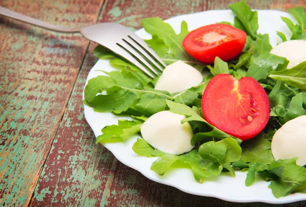 Groene salade gemaakt van arugula, tomaten, kaas mozzarella ballen en sesam op bord — Stockfoto