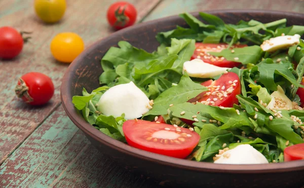 Groene salade gemaakt van arugula, tomaten, kaas mozzarella ballen en sesam op bord — Stockfoto