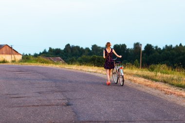 Genç kadın bisiklet ile yolda yürürken.