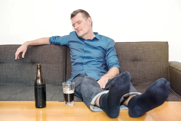 Человек спит на диване с бутылкой пива на столе — стоковое фото