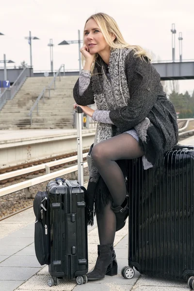 Женщина сидит на своем чемодане на вокзале — стоковое фото