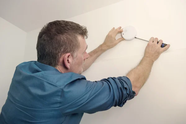 Handsome man repairing a smoke detector — Stock Photo, Image