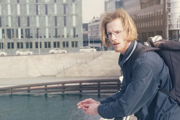 Young man with backpack standing by a bridge — Stock Photo, Image