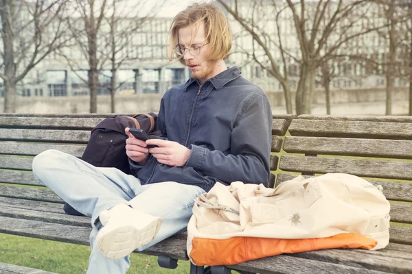 Jongeman zit op bankje en zijn telefoon te kijken — Stockfoto