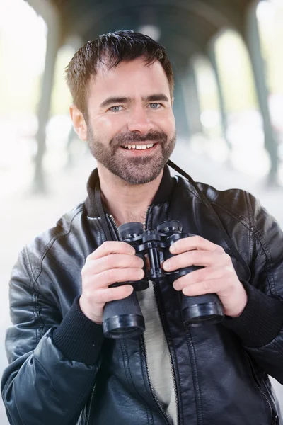 Homem segurando binóculos e sorrisos — Fotografia de Stock