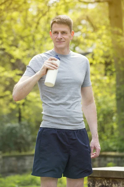 Man in shorts standing outdoors holding a bottle — Stock Photo, Image