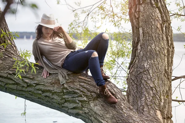 Jovem mulher sentada em uma árvore junto à água — Fotografia de Stock