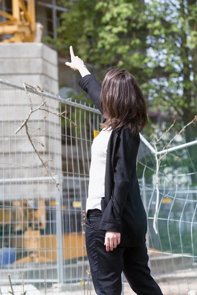 Vrouw permanent op de bouwplaats en wijzend op gebouw — Stockfoto