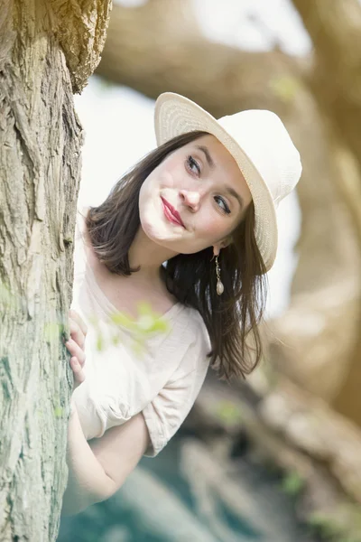 Jovem mulher com chapéu olhando em torno de uma árvore — Fotografia de Stock