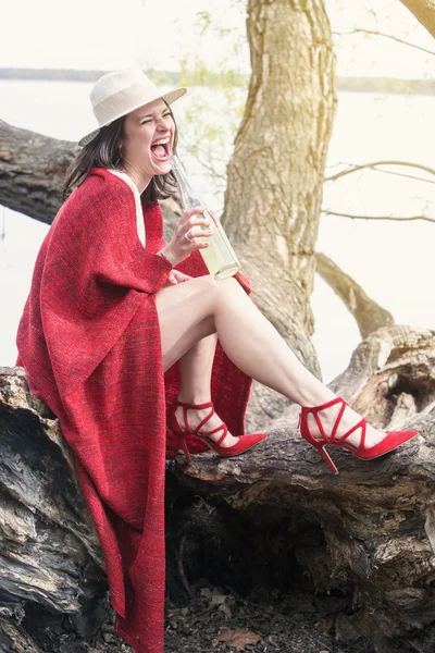 Vrouw zitten op een boom met een fles champagne — Stockfoto