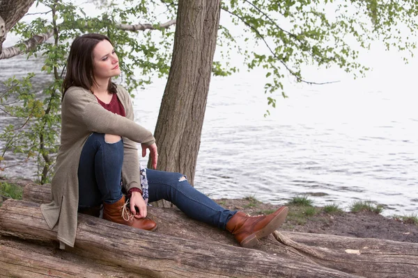 年轻女子坐在一棵树在水边 — 图库照片
