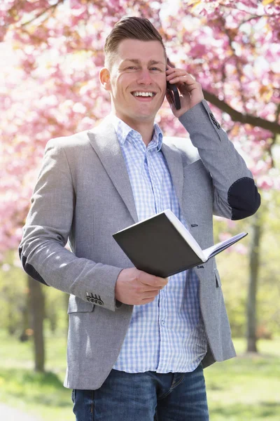 Forretningsmann i park med bok og telefon – stockfoto