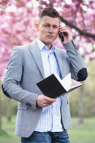 Empresário no parque com livro e telefone — Fotografia de Stock