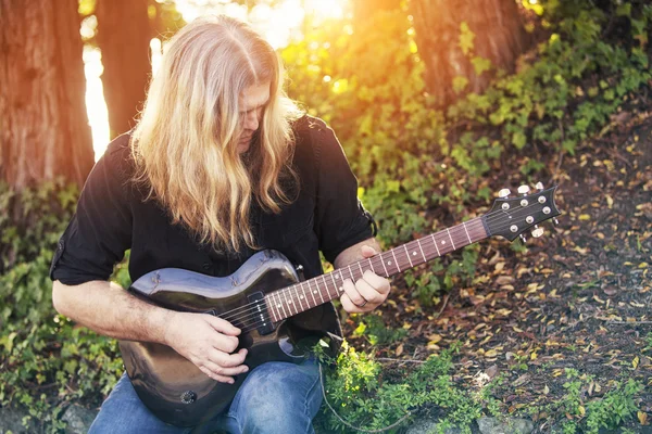 Homme aux cheveux longs jouant de la guitare dans un parc — Photo