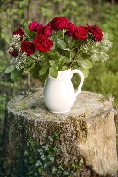 Ваза с красными розами на пне дерева — стоковое фото