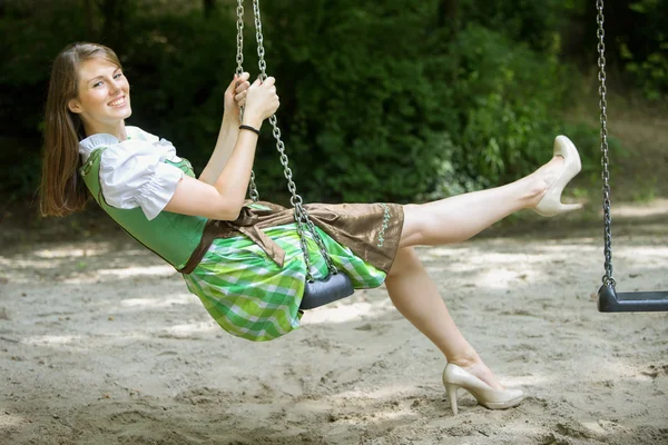 Kvinna i dirndl sitter på swing — Stockfoto