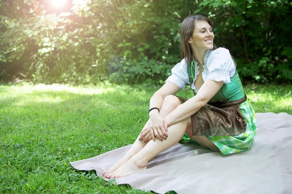 Jonge vrouw in dirndl zittend op de deken in gras — Stockfoto