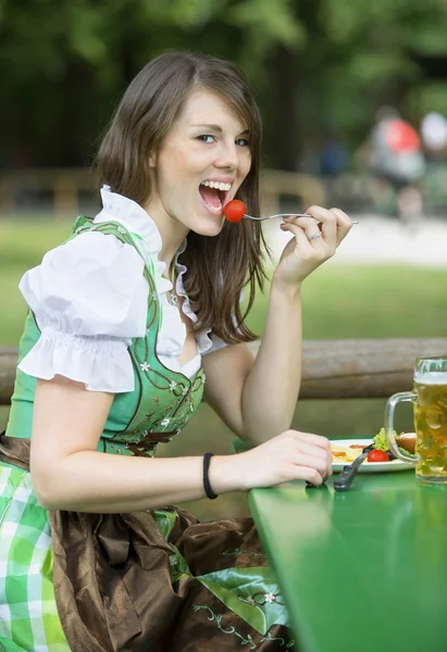 Frau im Dirndl sitzt draußen und isst — Stockfoto