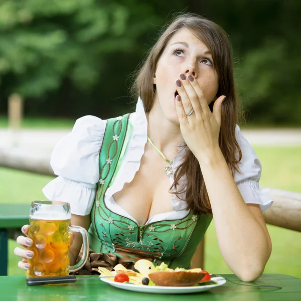 Woman in dirndl sitting at beer garden and is yawning — Stock Photo, Image