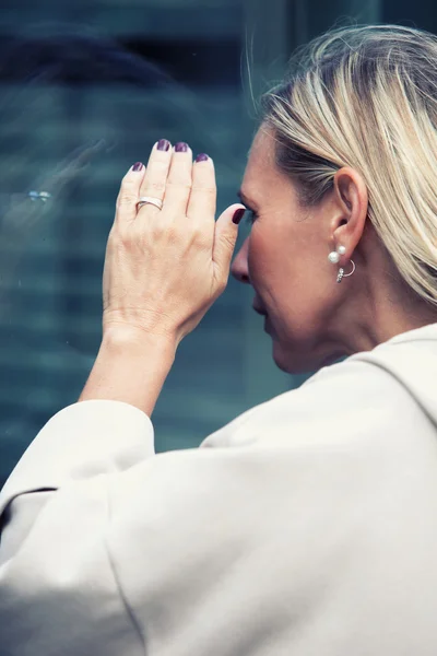 Blond kvinna som tittar genom ett fönster — Stockfoto