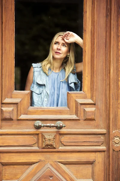 Donna che guarda attraverso la finestra di una porta di legno — Foto Stock