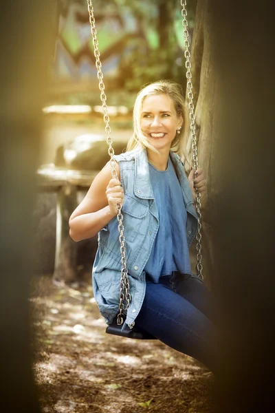 Blondine sitzt auf Schaukel auf Spielplatz — Stockfoto