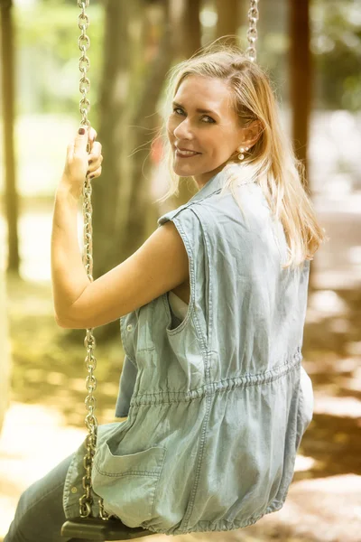 Mulher loira sentada no balanço no parque infantil — Fotografia de Stock