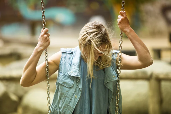 Mujer rubia sentada en columpio en el patio de recreo — Foto de Stock