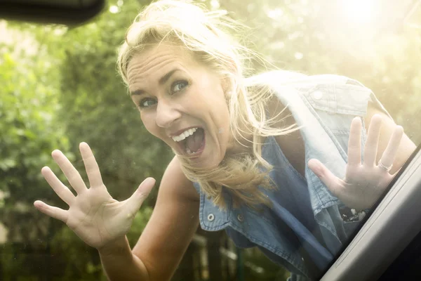 Vrouw op zoek binnen auto en het maken van een grappig gezicht — Stockfoto