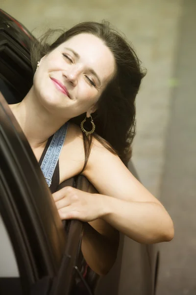 Jonge vrouw leunend uit auto en glimlachen — Stockfoto