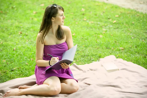 Jovem mulher sentada no parque e escrita — Fotografia de Stock