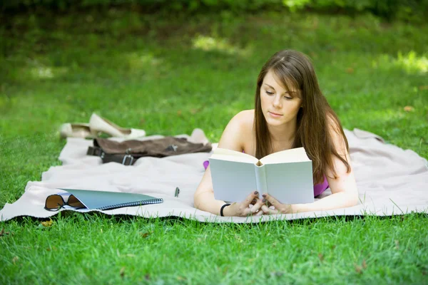 Mujer joven acostada en el parque y leyendo un libro — Foto de Stock